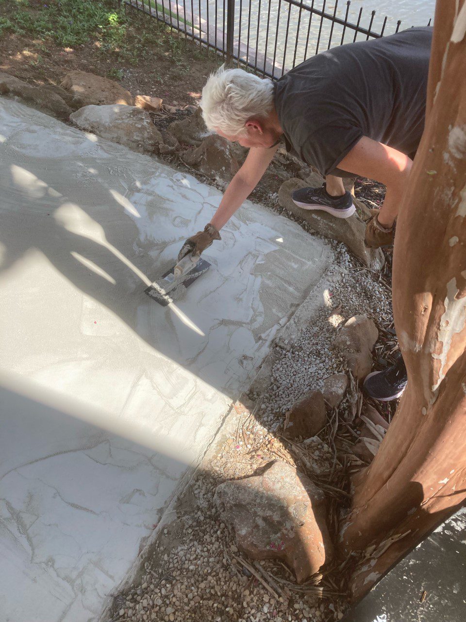 A woman hand-troweling her DIY poured concrete patio, intentionally creating texture for a unique and personalized outdoor space.