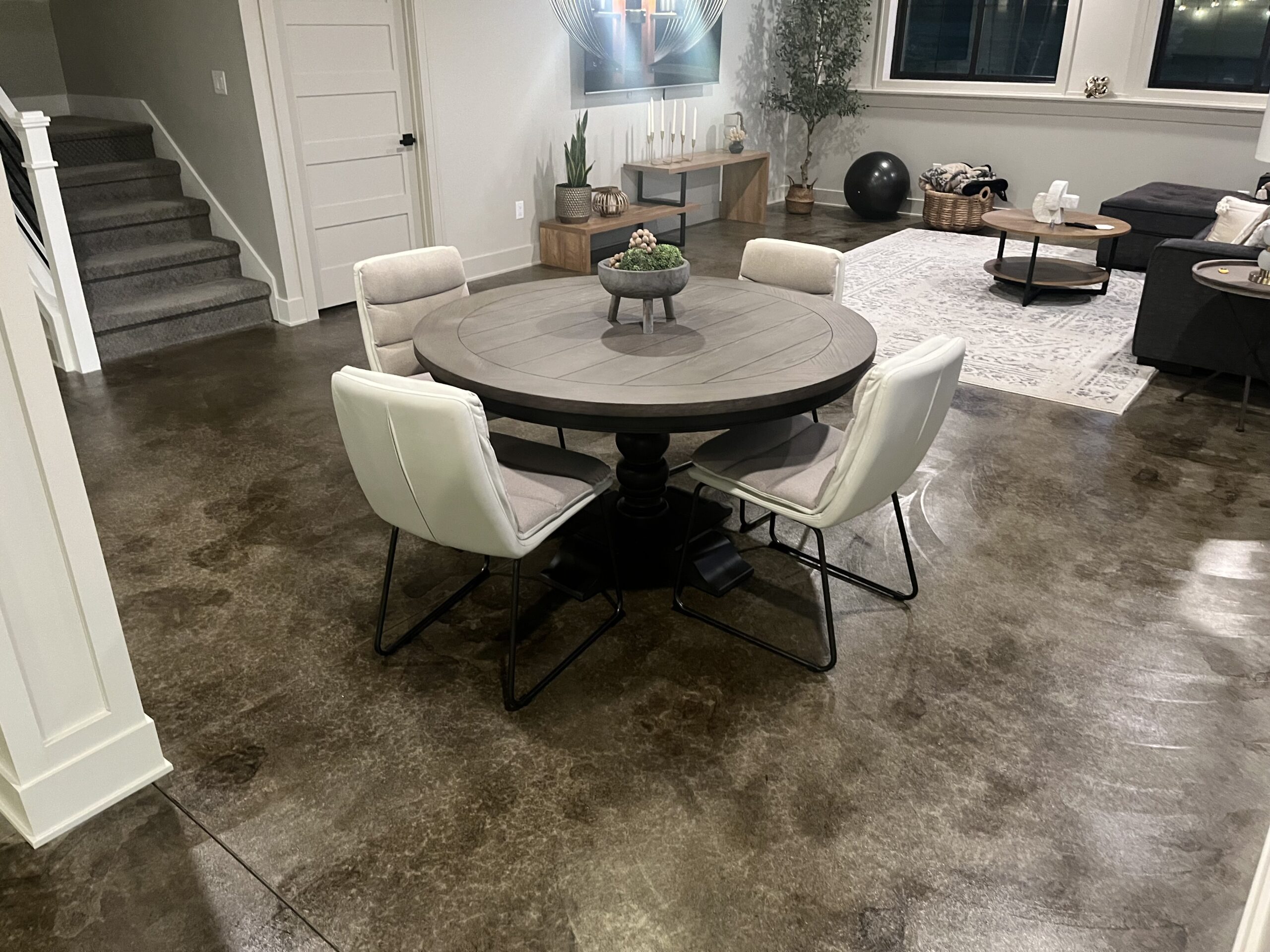 A living and dining area in a basement with a Molasses ColorWave stained concrete floor, highlighting the smooth, dark brown finish that enhances the furniture and décor of the space.