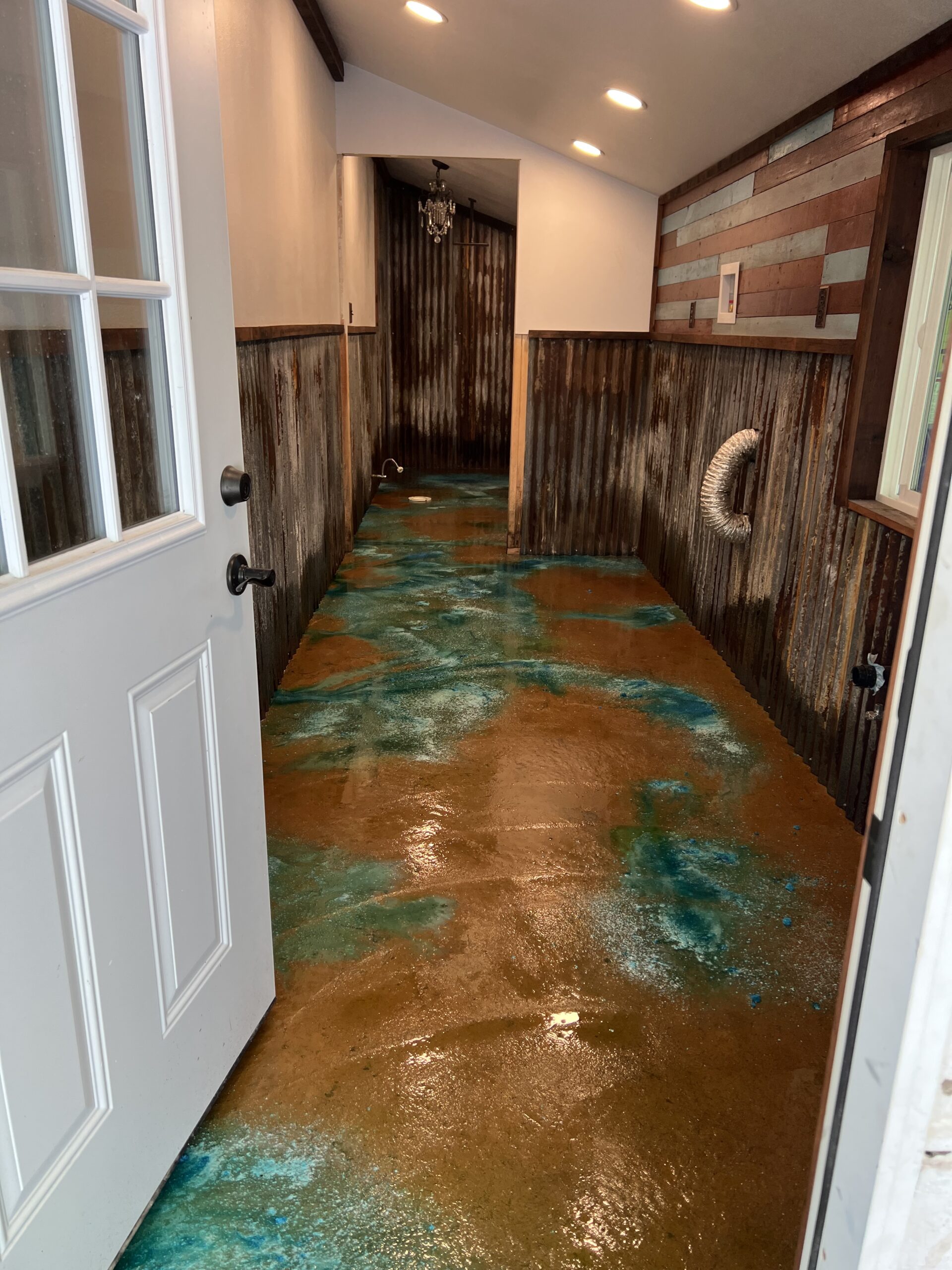 A multipurpose room with a stained concrete floor featuring vibrant azure blue and English red patterns, surrounded by corrugated metal walls.