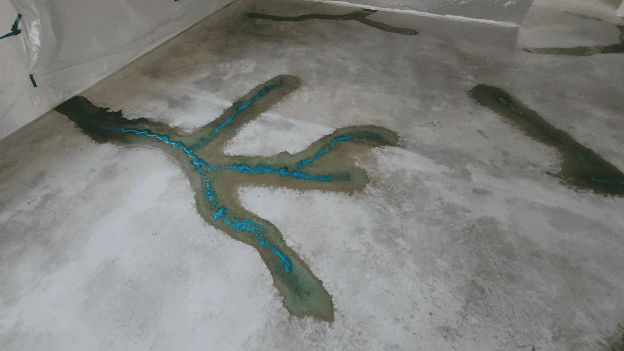 Concrete floor with Miracle Gro granules spread in a pattern, with blue acid stain reacting on the surface, creating vibrant blue areas