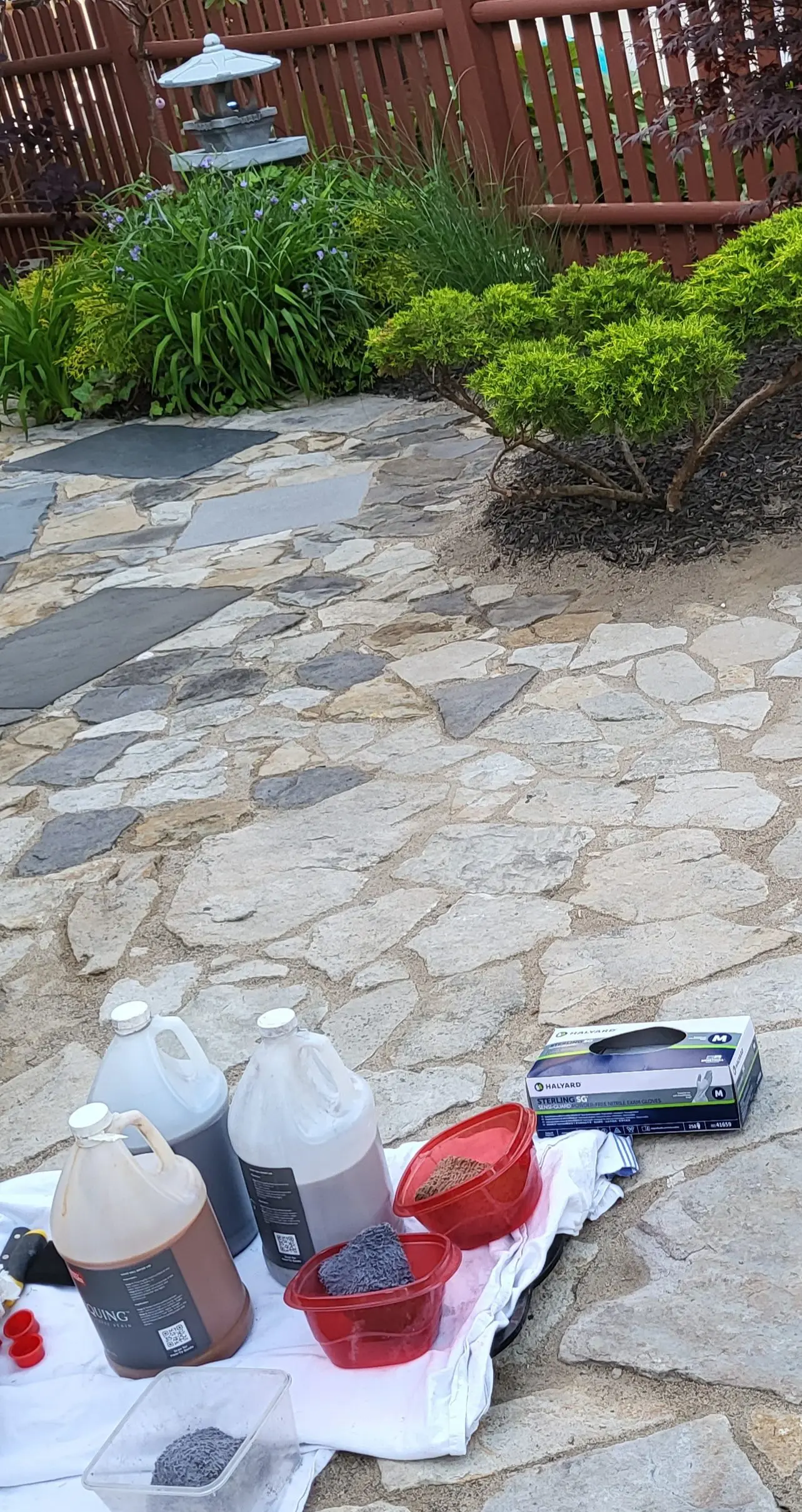 A DIY patio stone design in progress, featuring individual stones being meticulously hand-stained with sponges, using various concrete stain colors to achieve a realistic slate appearance.