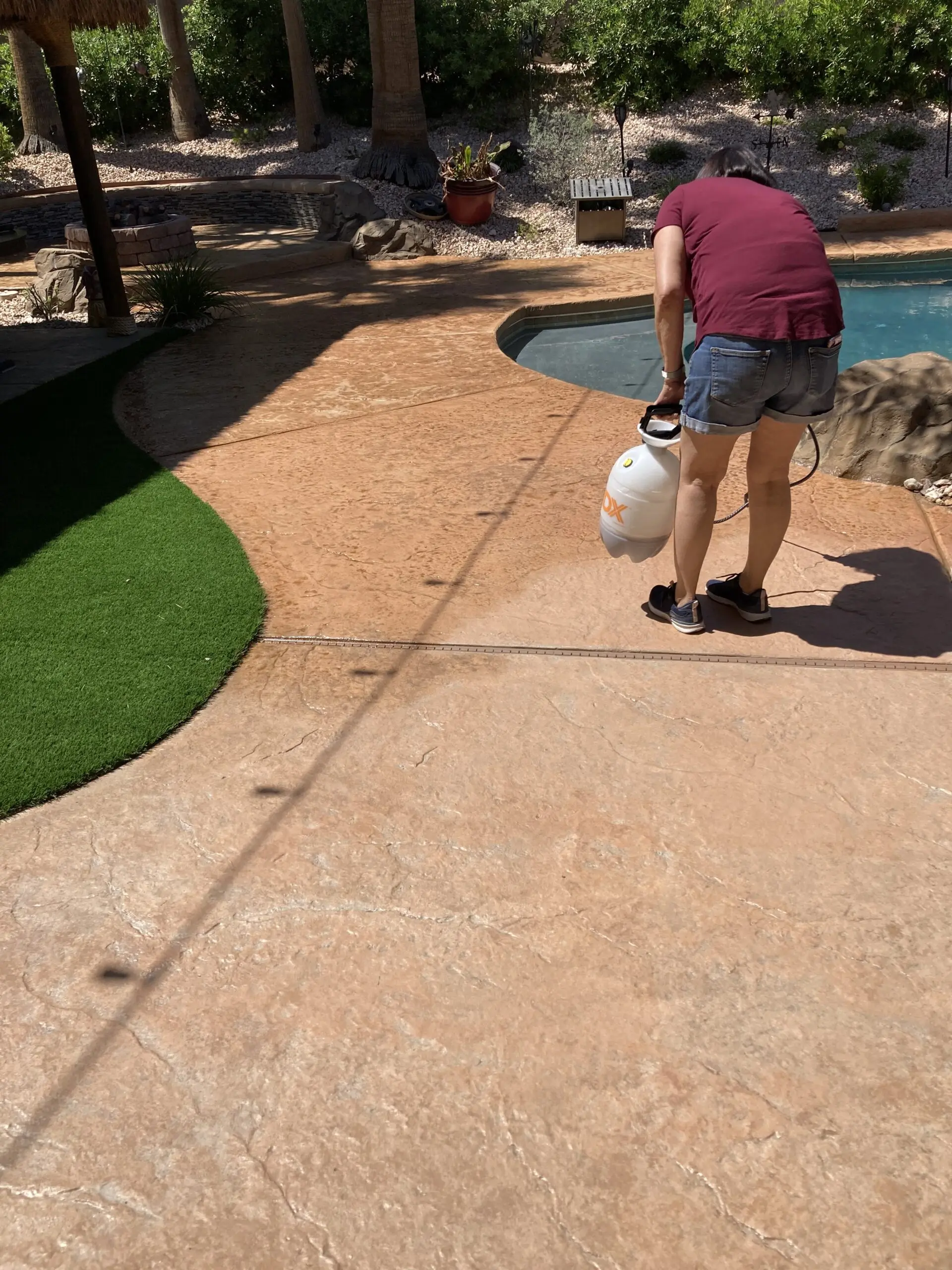 A person applying Café Royale Antiquing stain on a stamped concrete pool deck using a pump sprayer