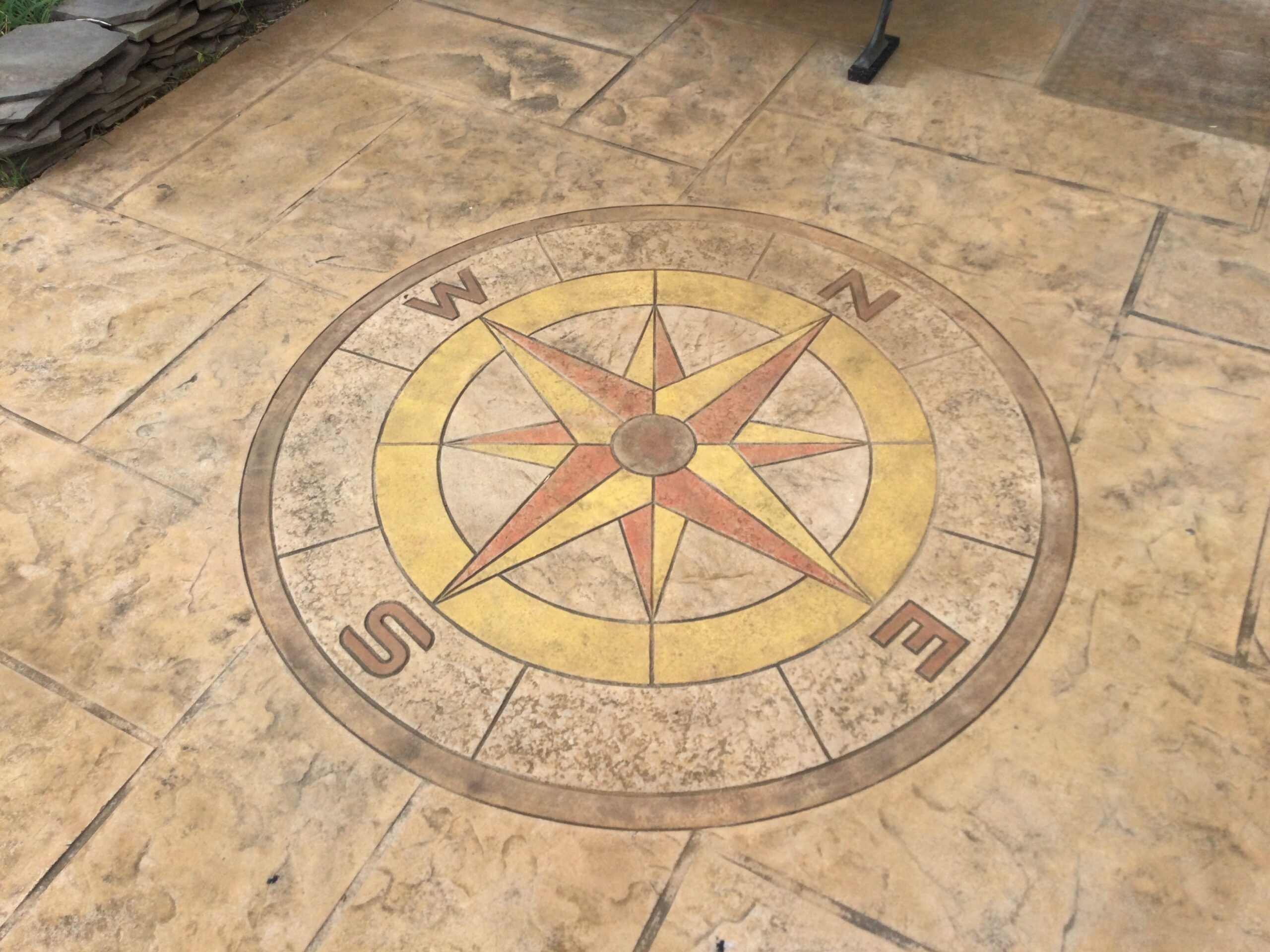 The faded stamped compass rose on the concrete driveway, barely visible due to weathering