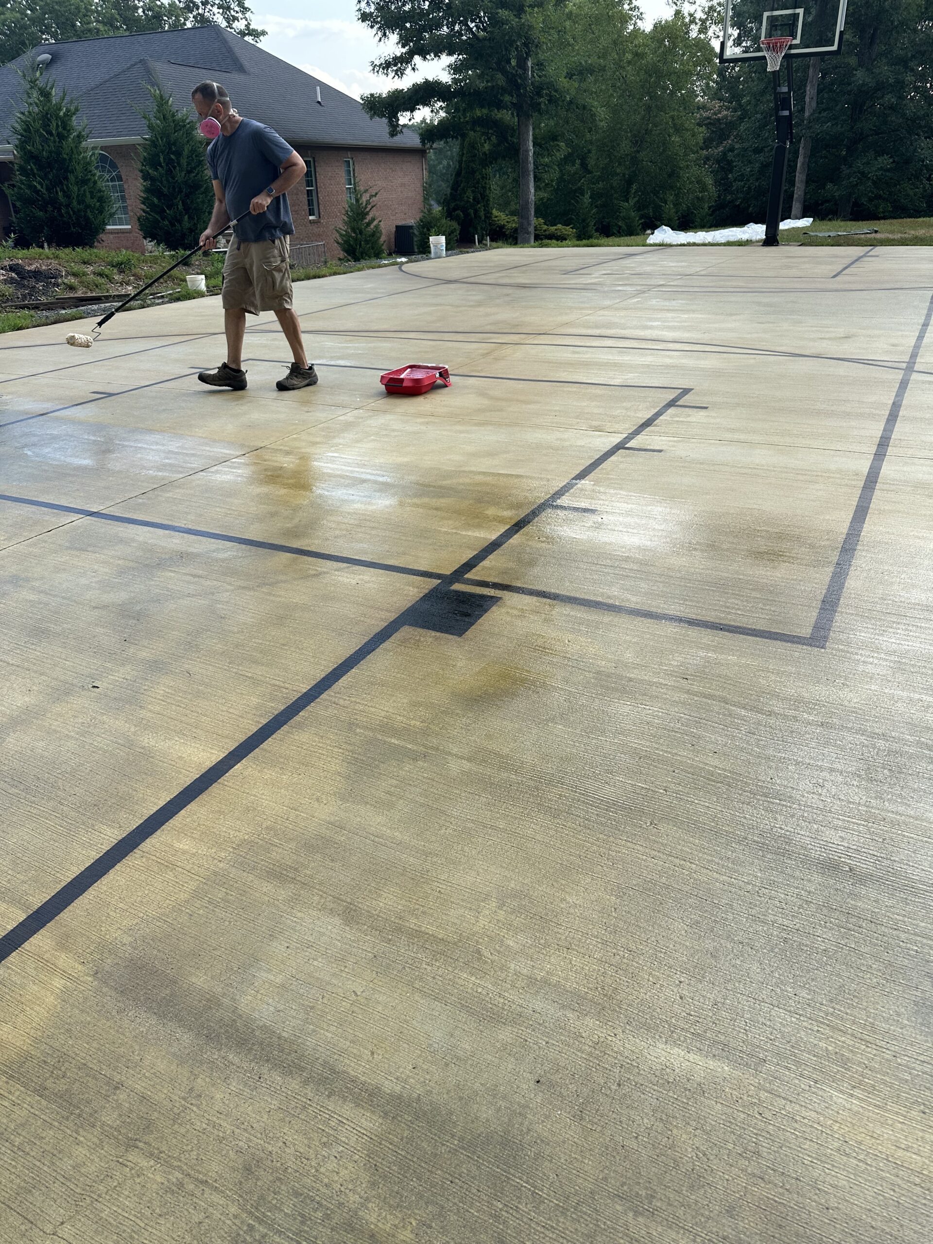 A man applying a sealer to the basketball court surface using a roller, ensuring the stain is protected