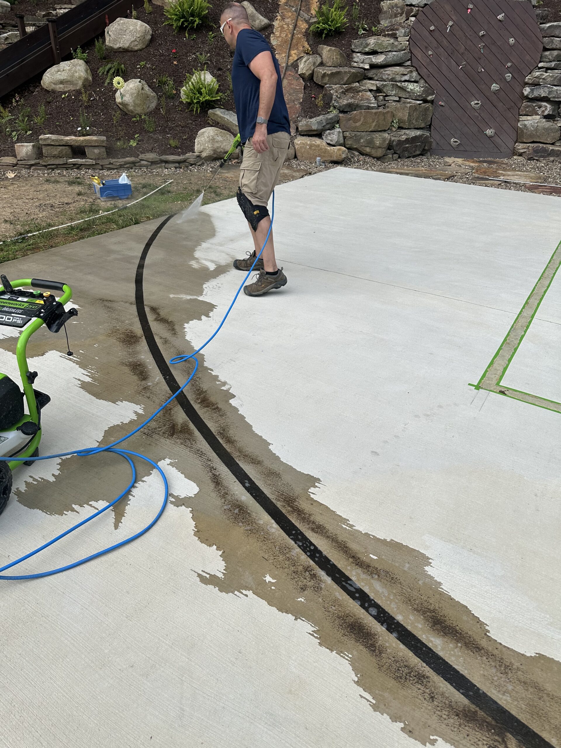 A man rinsing off the DecoGel Coffee Brown stain from the lines of a concrete basketball court.