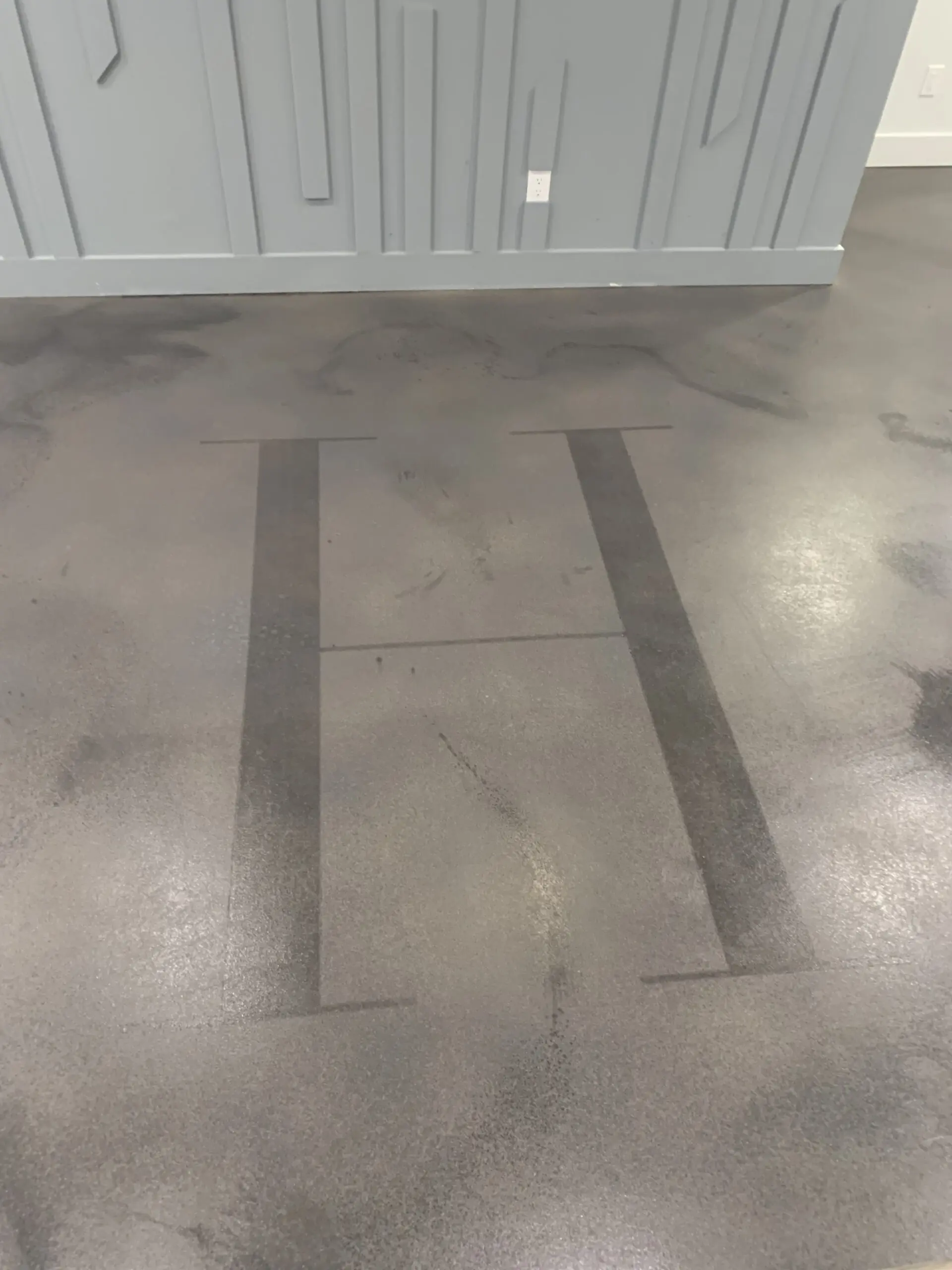 A concrete floor with a large, stylized letter "H" stenciled onto the surface, set against a faux polished finish with subtle color variations.