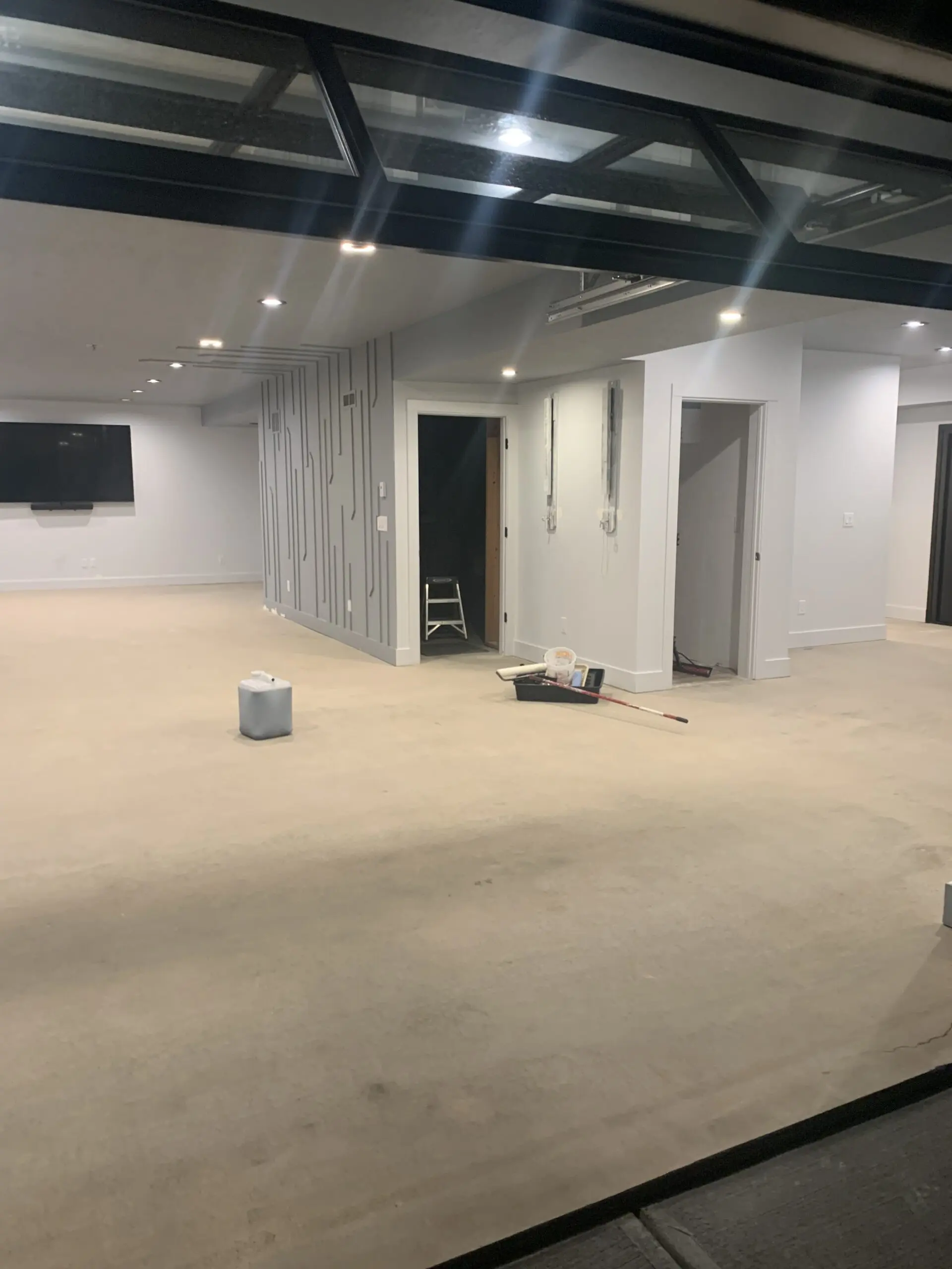 A clean, prepared concrete floor in a room with light-colored walls and ceiling, ready for stain application. A container and some tools are visible on the floor.