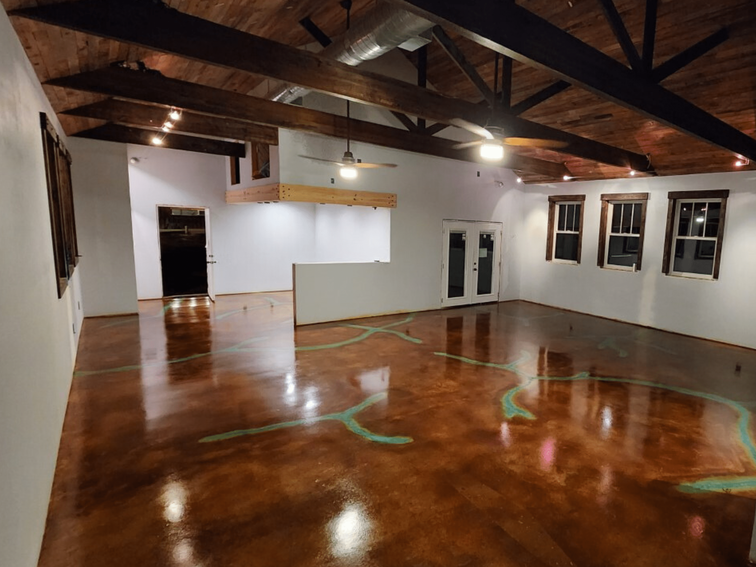 A spacious residential interior with high ceilings and exposed beams, featuring a fully stained concrete floor with intricate patterns in Azure Blue, Black, and Cola