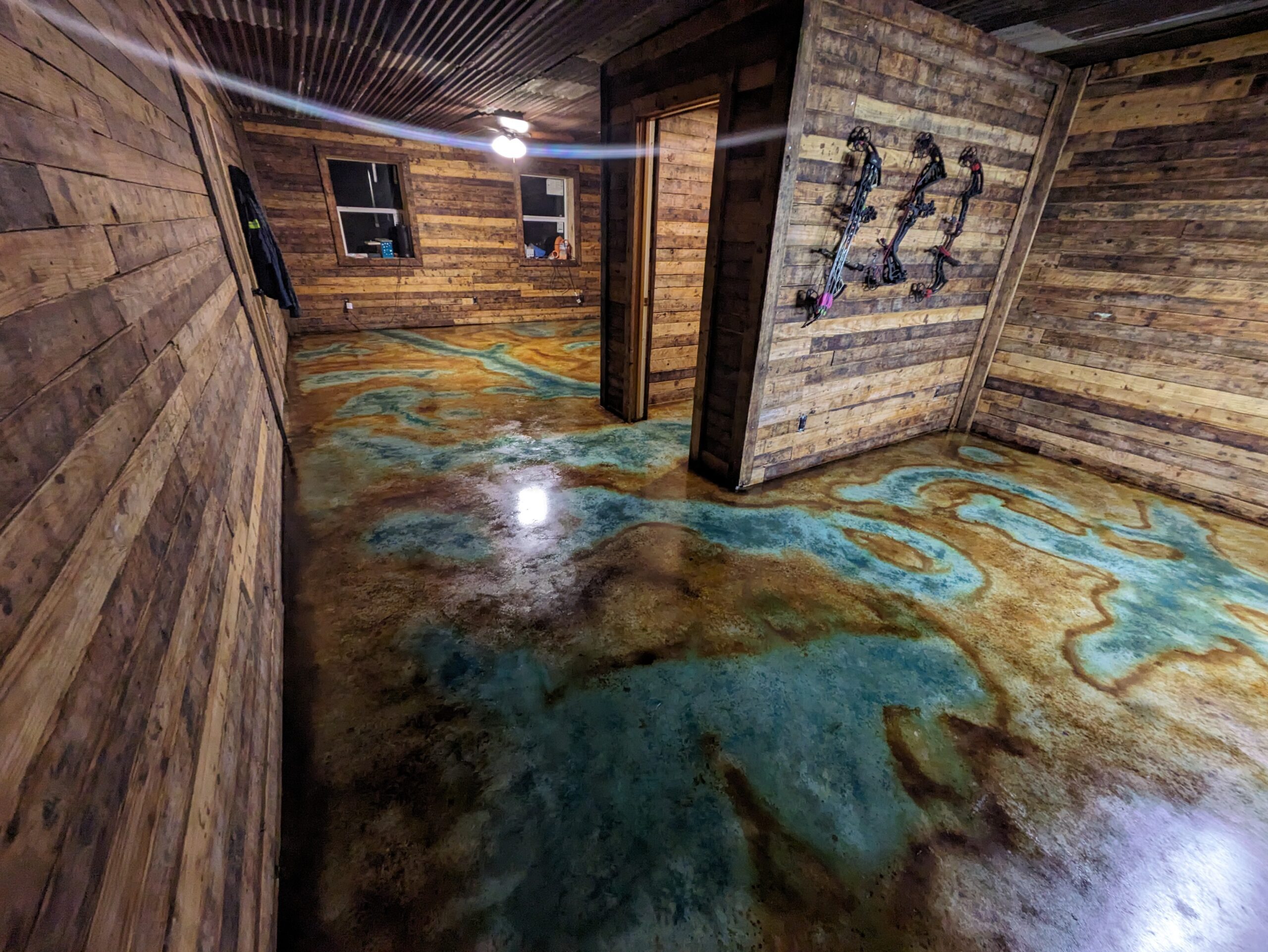 An interior view of a room with a concrete floor artistically stained with hues of Coffee Brown, Malayan Buff, and Seagrass, evoking the appearance of a natural, sandy riverbed