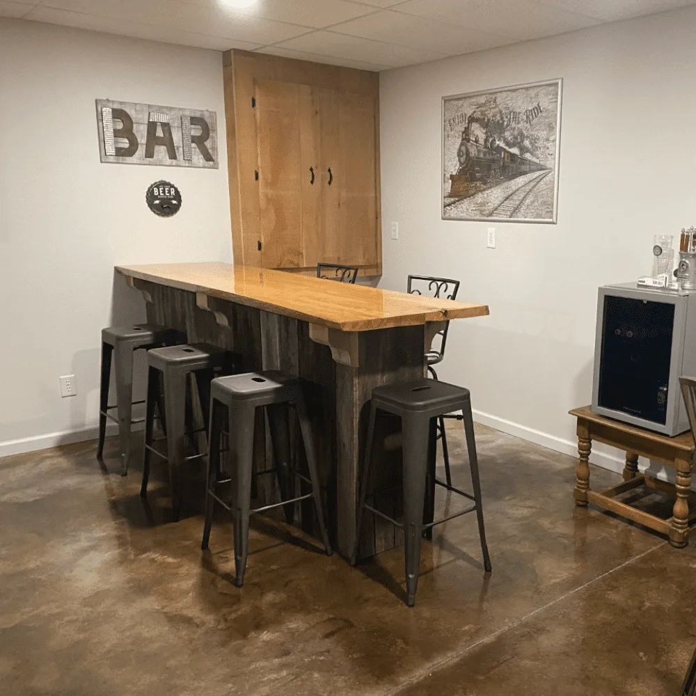 A home bar setup in a basement with acid-stained concrete floors in Coffee and Desert Amber, providing a rich, warm ambiance complemented by rustic furniture and themed decor