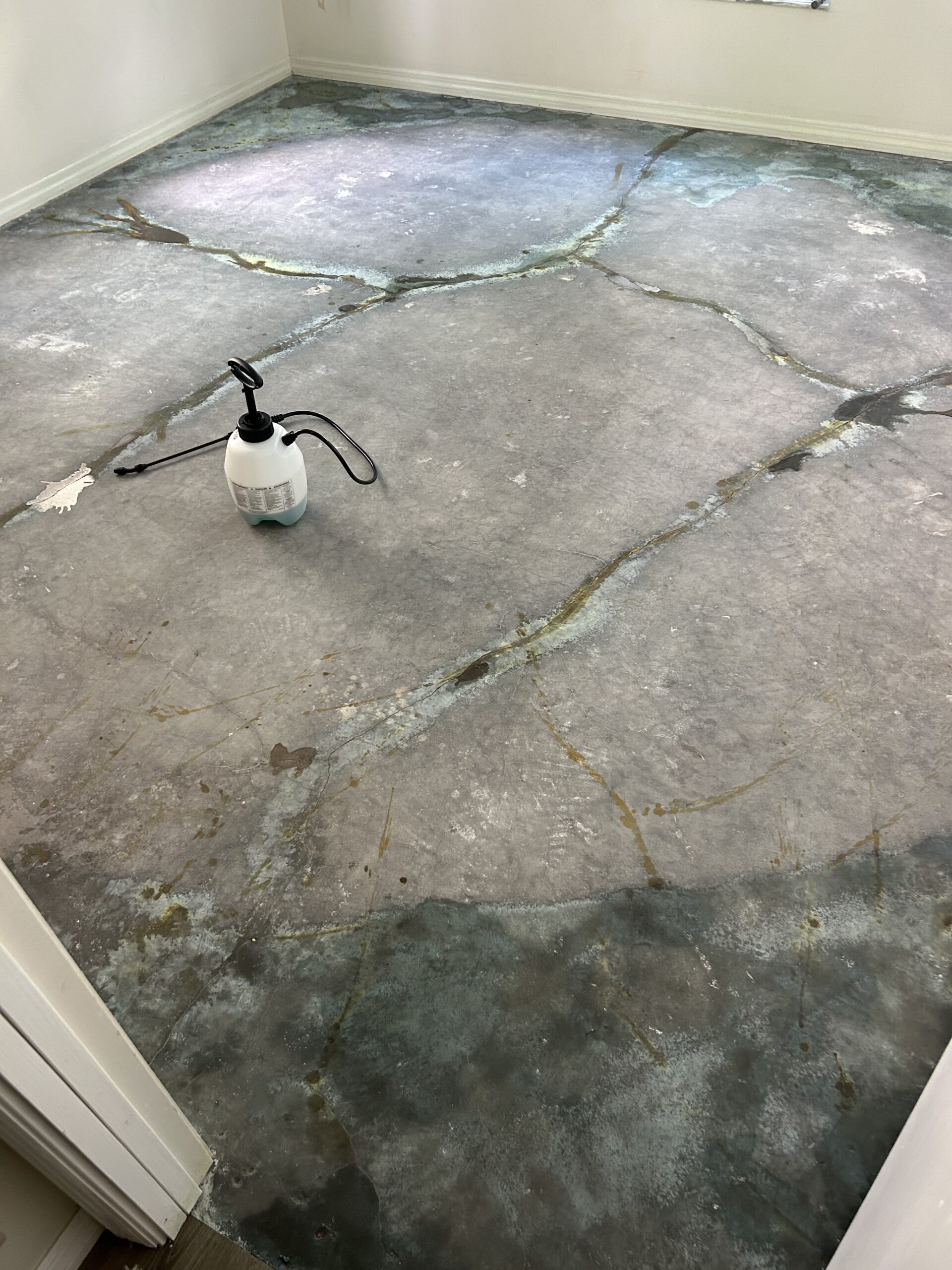 Accented cracks on the concrete floor using different colors, with Azure Blue stain applied to the corners, showing the progress of the staining process.