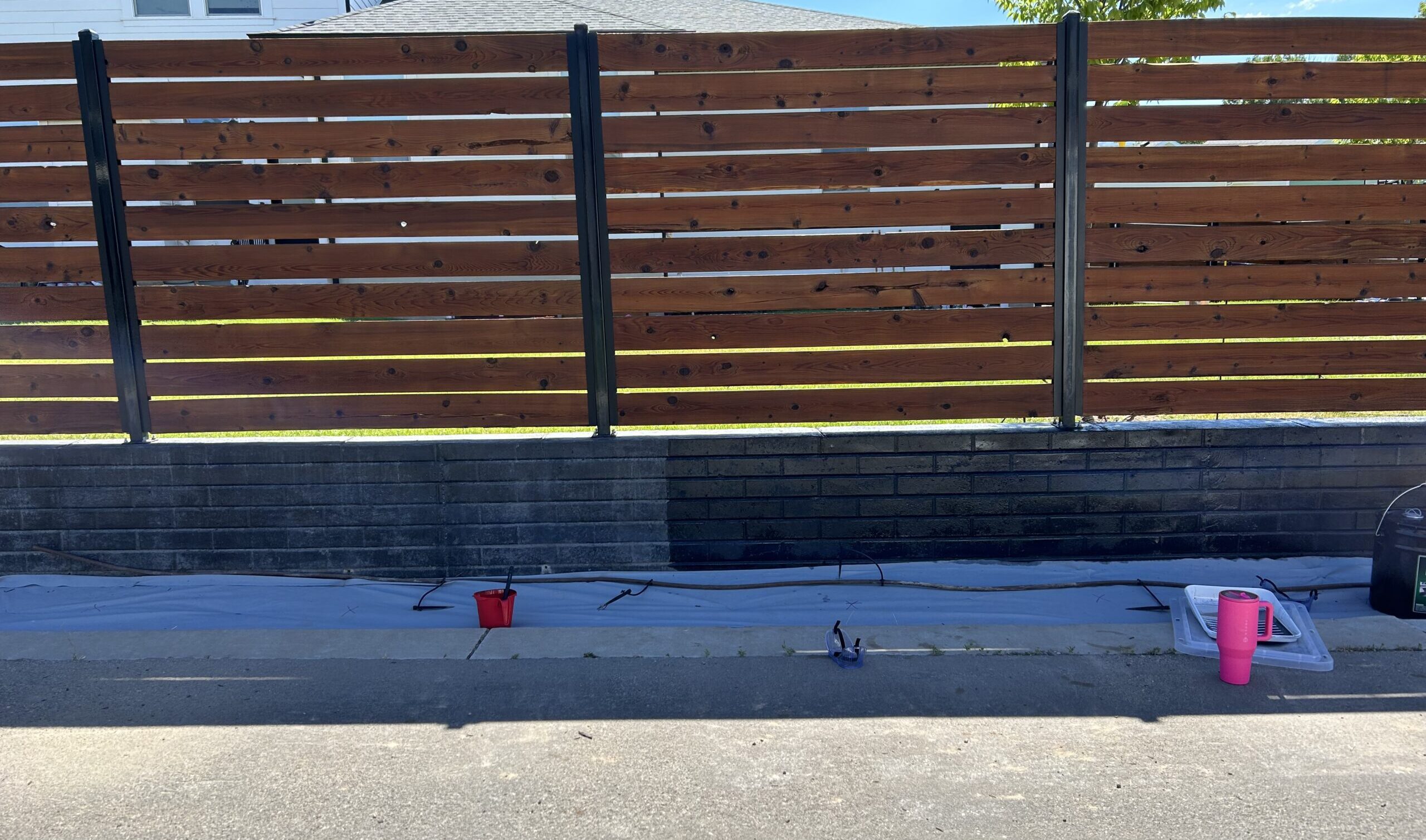 A black concrete wall with a wooden fence above, during staining