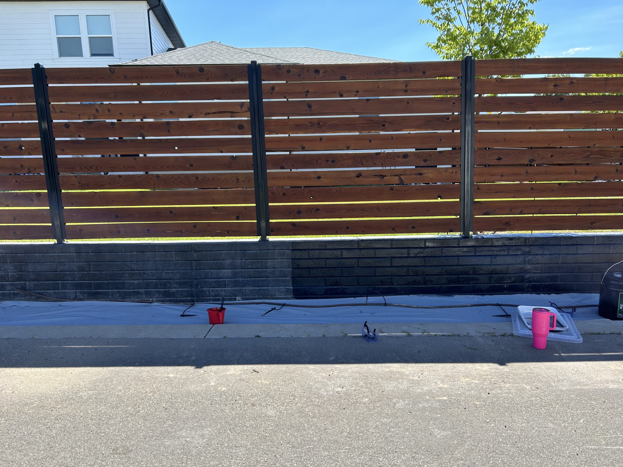 A black concrete wall with a wooden fence above, during staining