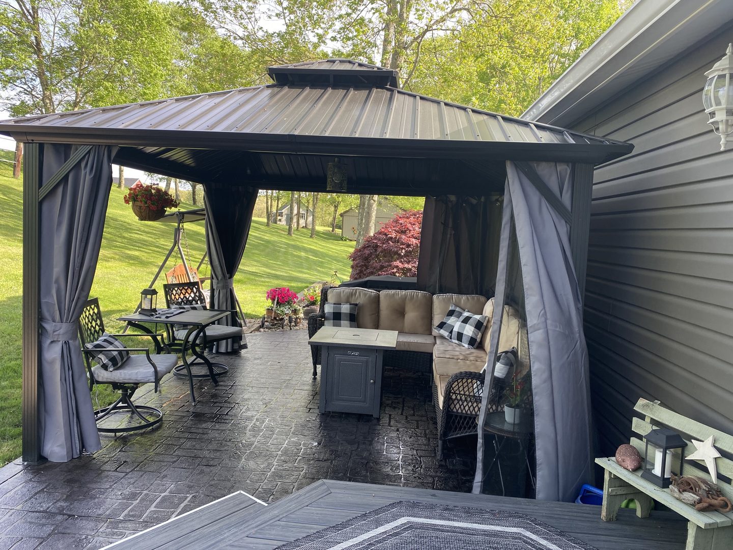 A cozy outdoor patio under a gazebo with comfortable seating and a stamped concrete floor stained in a sleek black finish