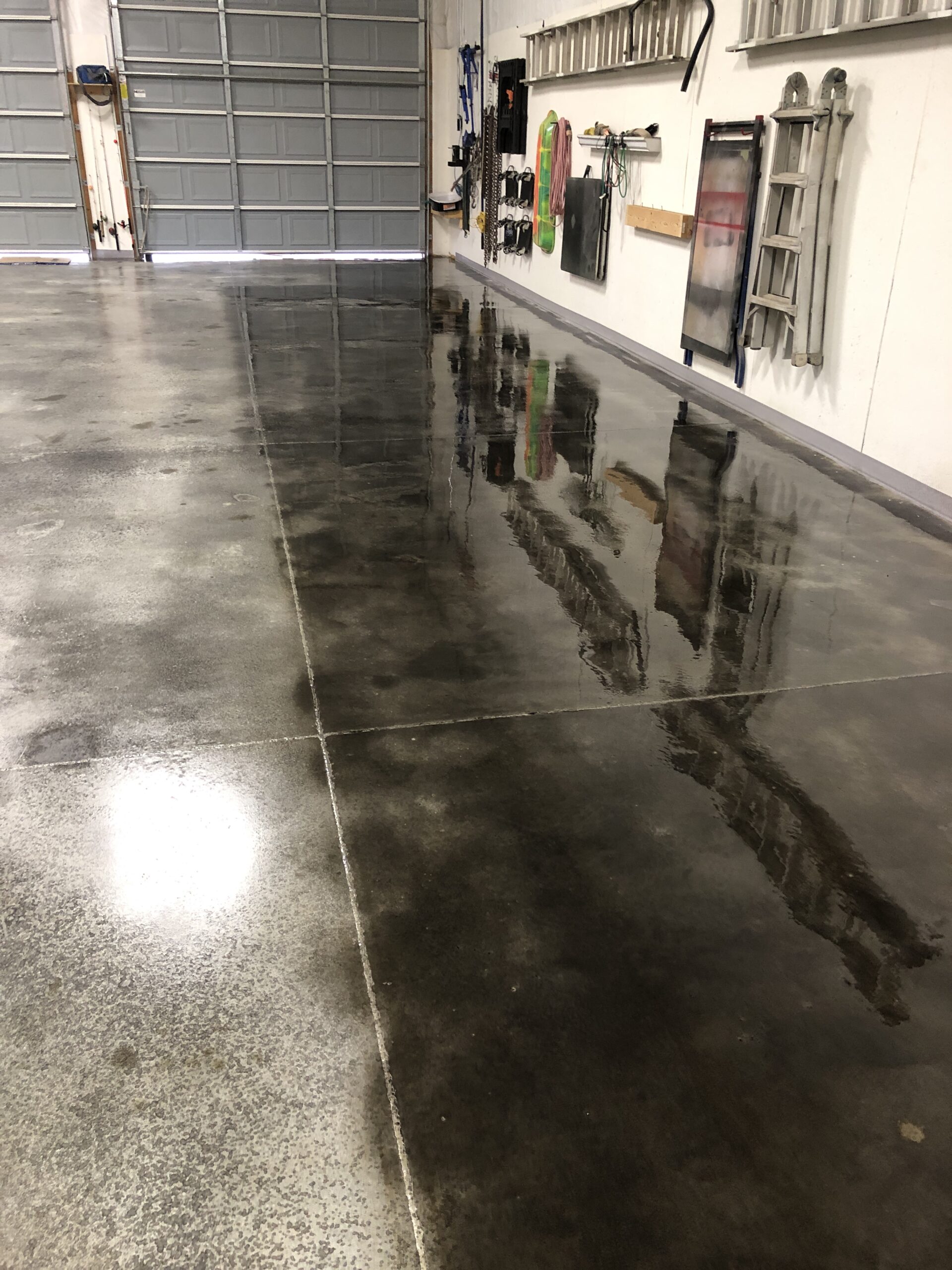 Barn shop floor after second coat of black concrete stain, showing improved uniformity.