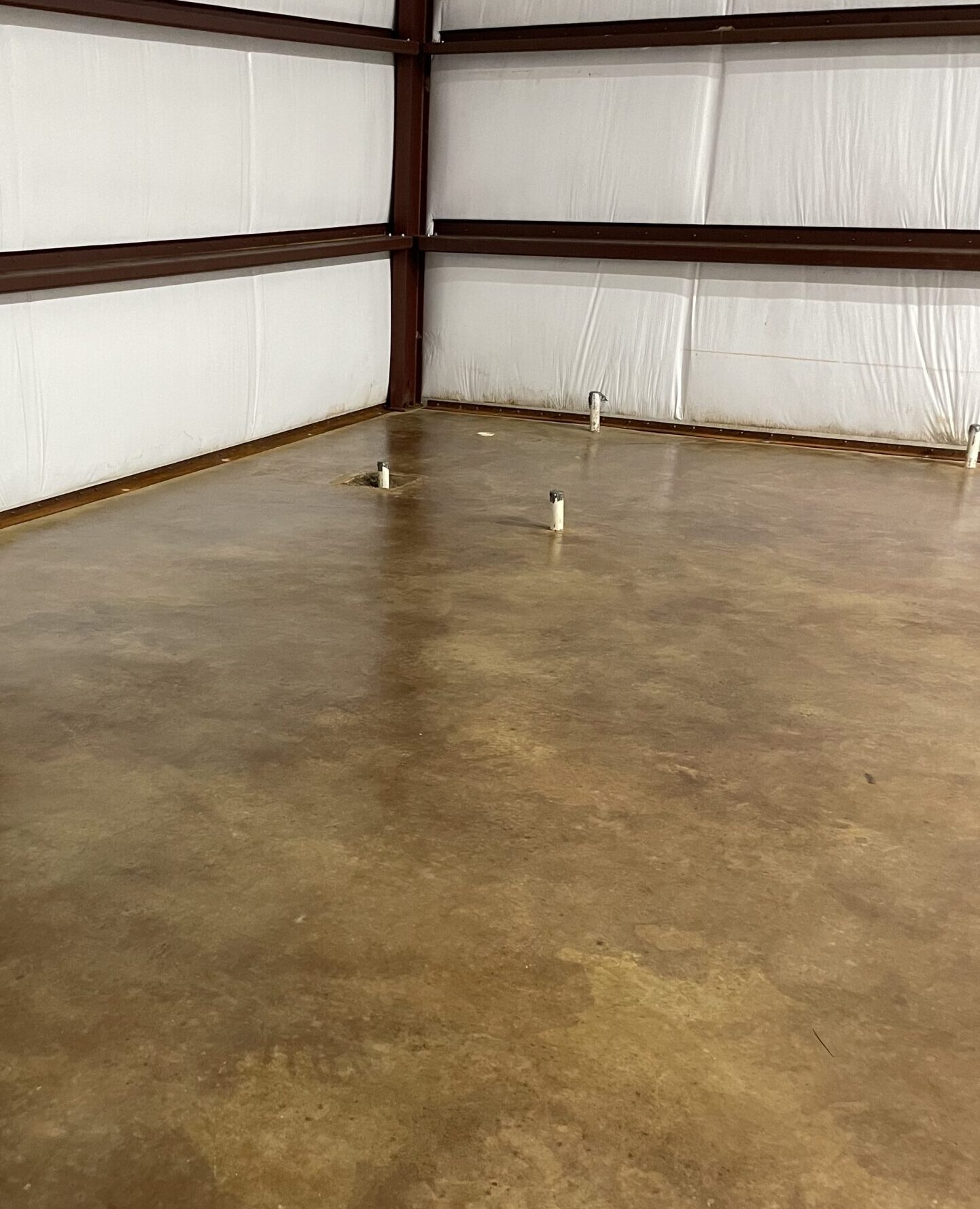 A polished concrete floor in a large, unfinished space with soft brown and tan tones created by acid staining