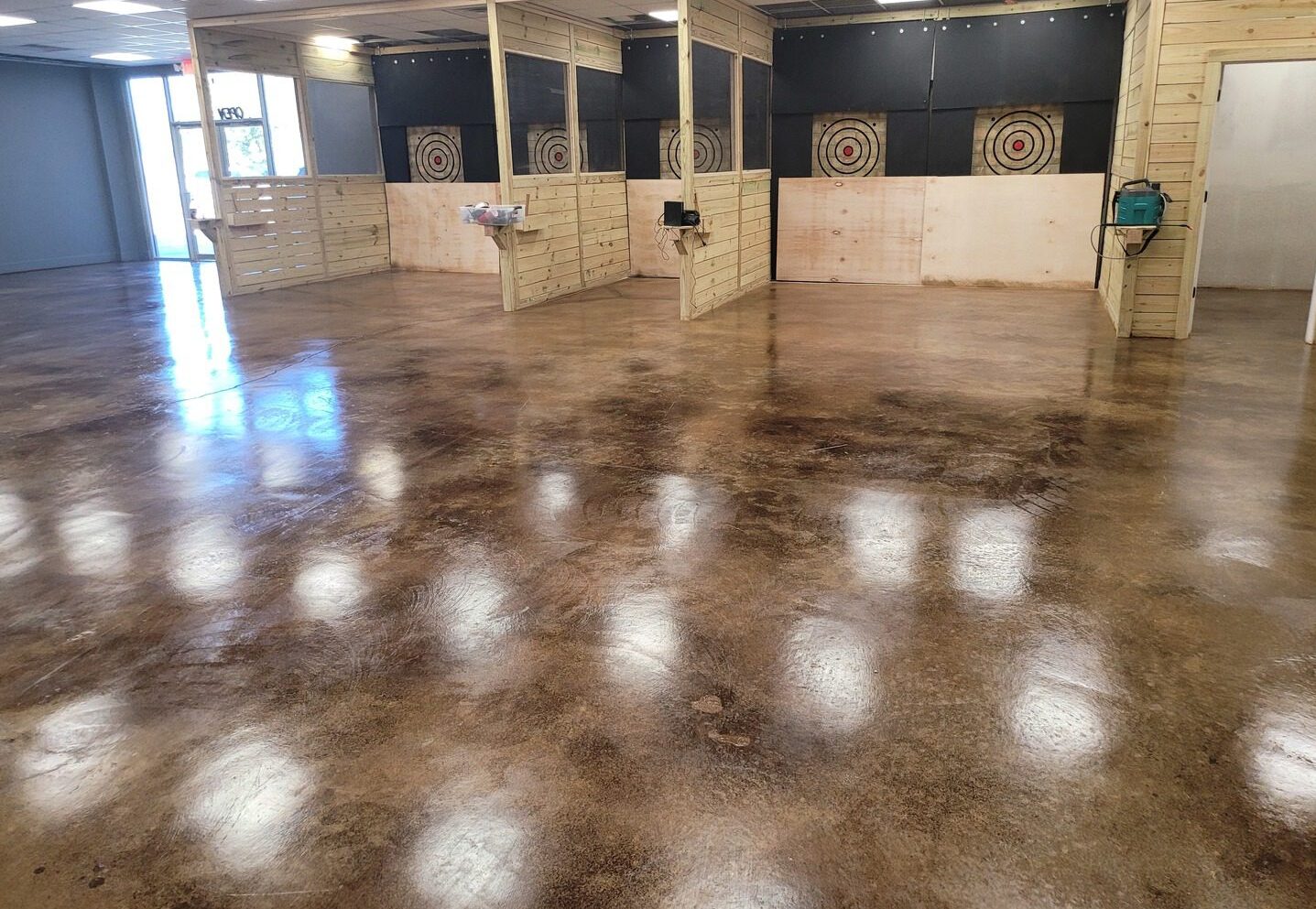 commercial concrete floor featuring a coffee brown acid stain, creating a rich and warm leather-like finish, complemented by wooden accents and target boards on the walls.