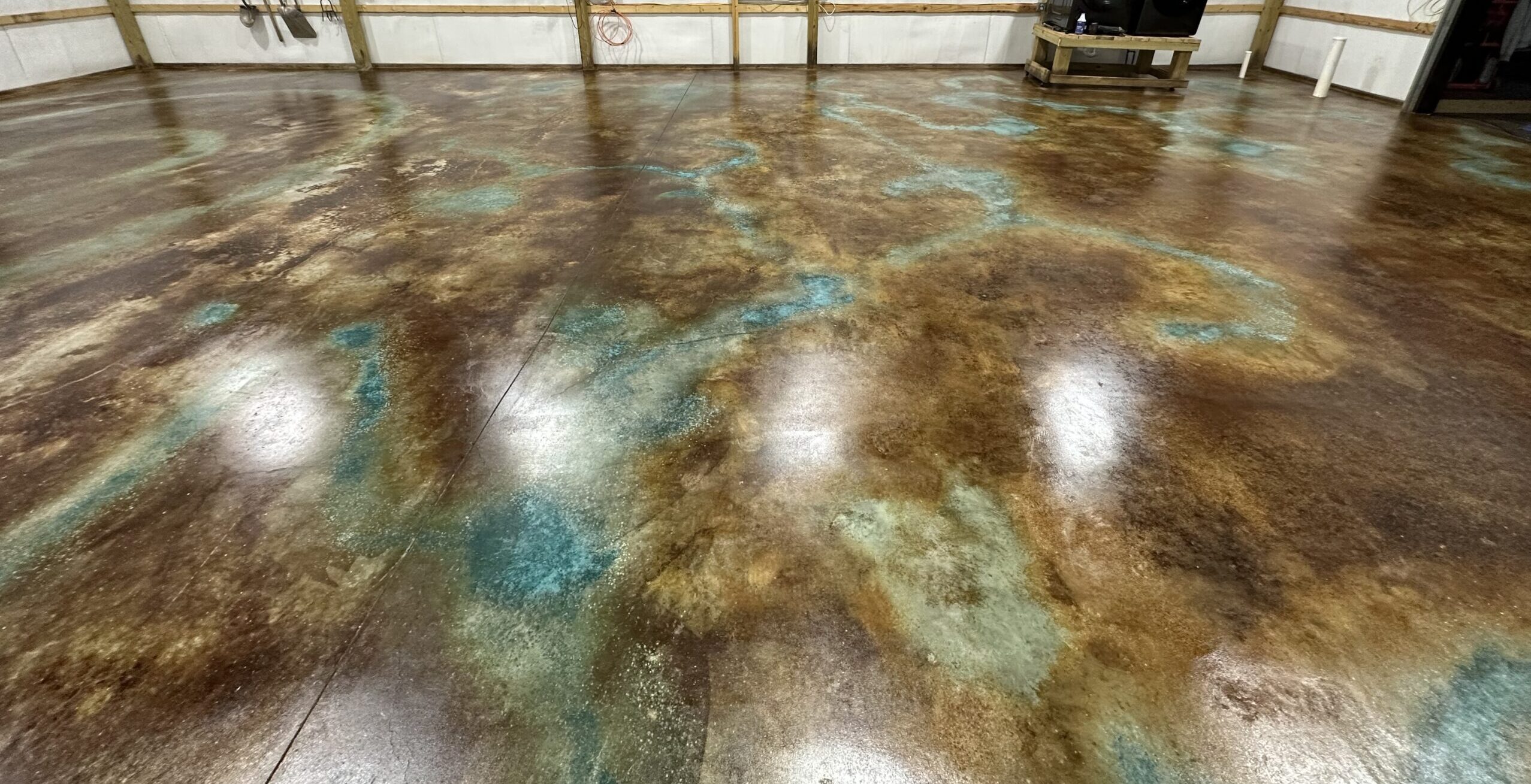 A spacious warehouse interior transformed into a polished floor with an intricate blend of azure blue, coffee brown, and English brown acid stains creating a rich, marbled effect.