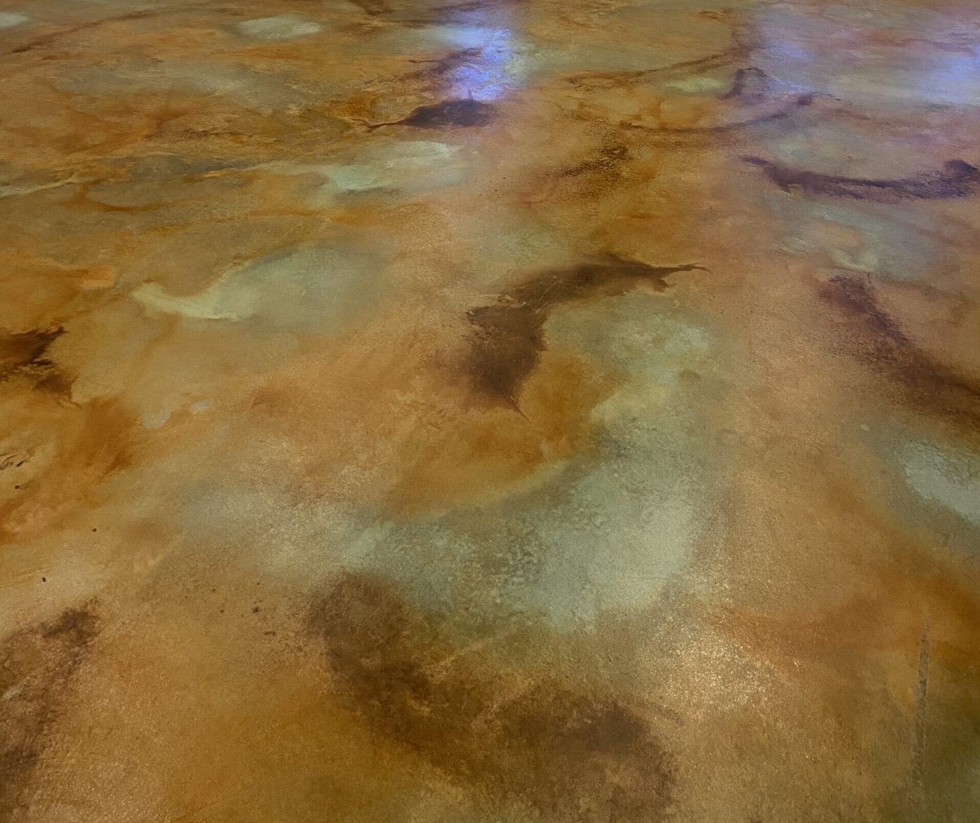 A room with a polished concrete floor featuring a blend of earthy brown, amber, and light green tones from acid staining, creating a marbled effect.