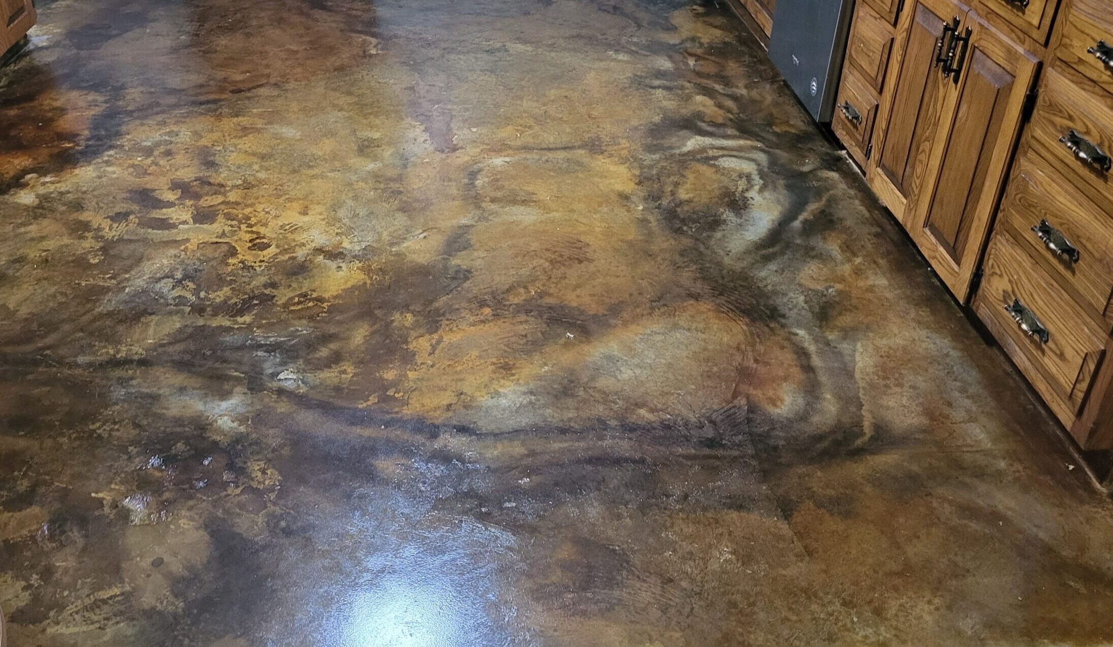 A kitchen floor with a rich blend of brown and amber tones, featuring a marbled effect achieved through acid staining