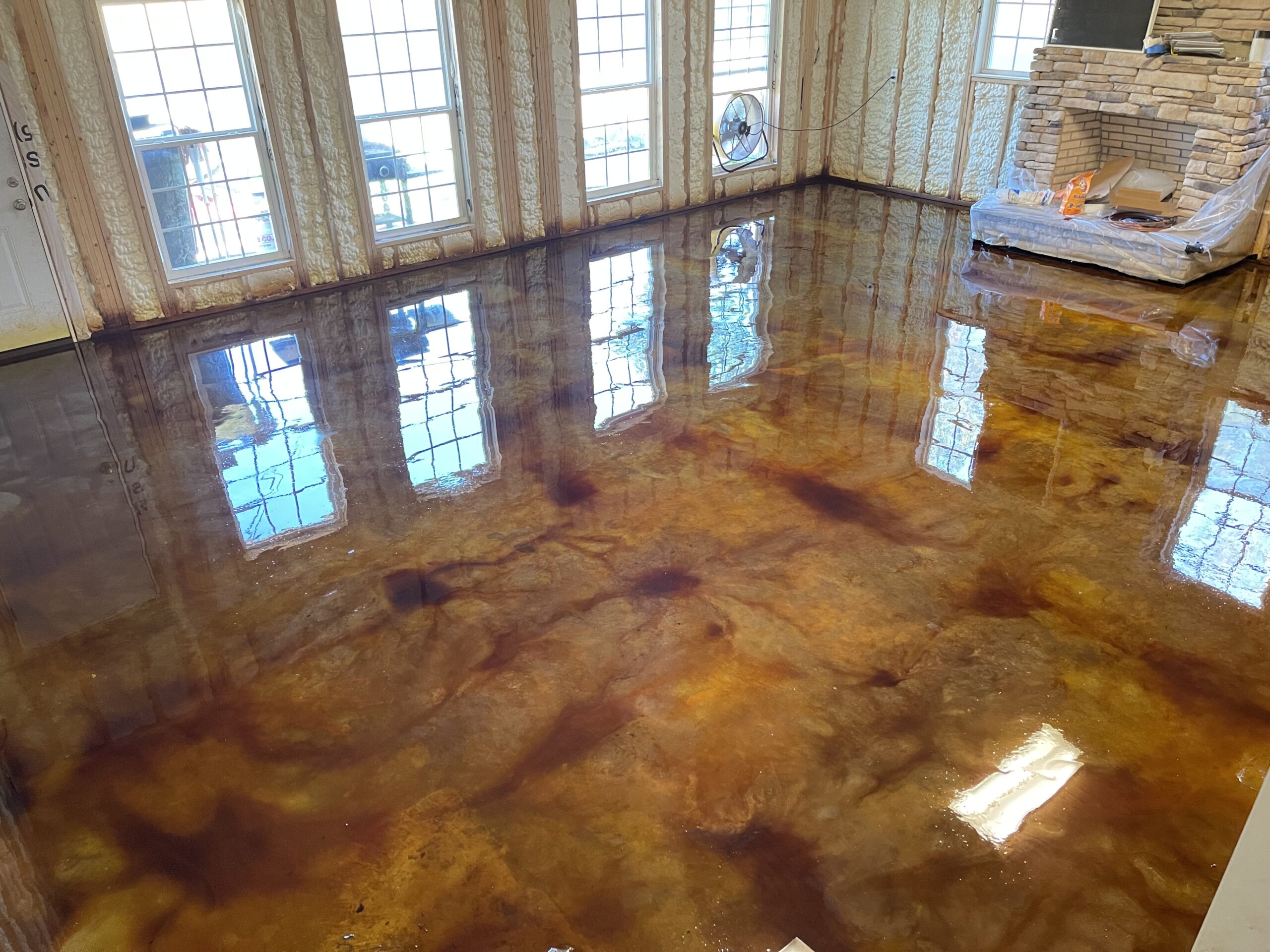 A living room under construction with reflective EverStain Black and Coffee Brown-stained floors, creating a glossy, leather-like finish.