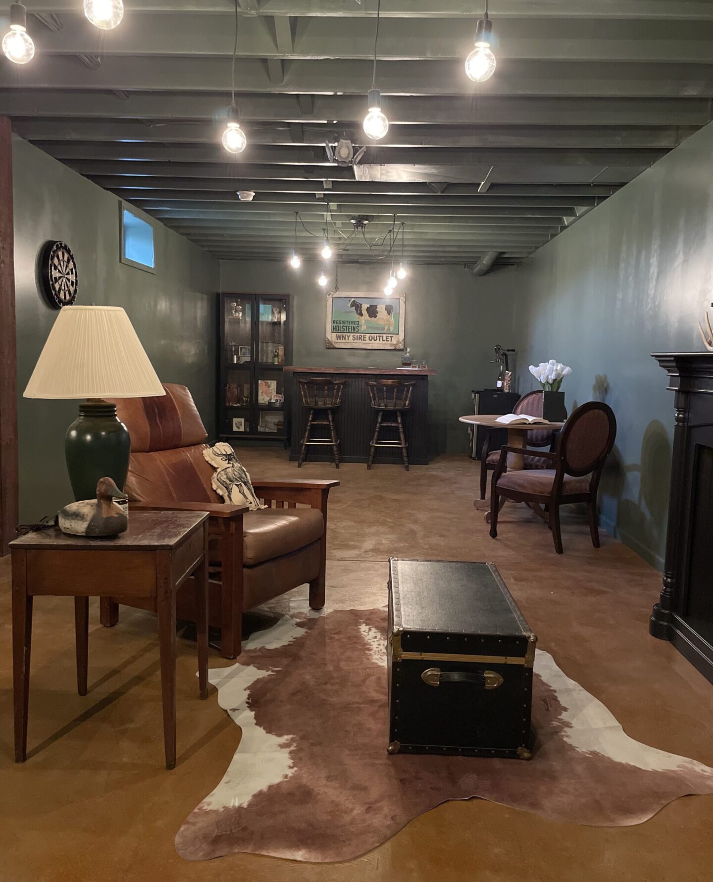 A cozy basement whiskey bar with polished concrete floors in warm brown tones, featuring rustic leather furniture, a cowhide rug, and vintage decor under soft hanging lights