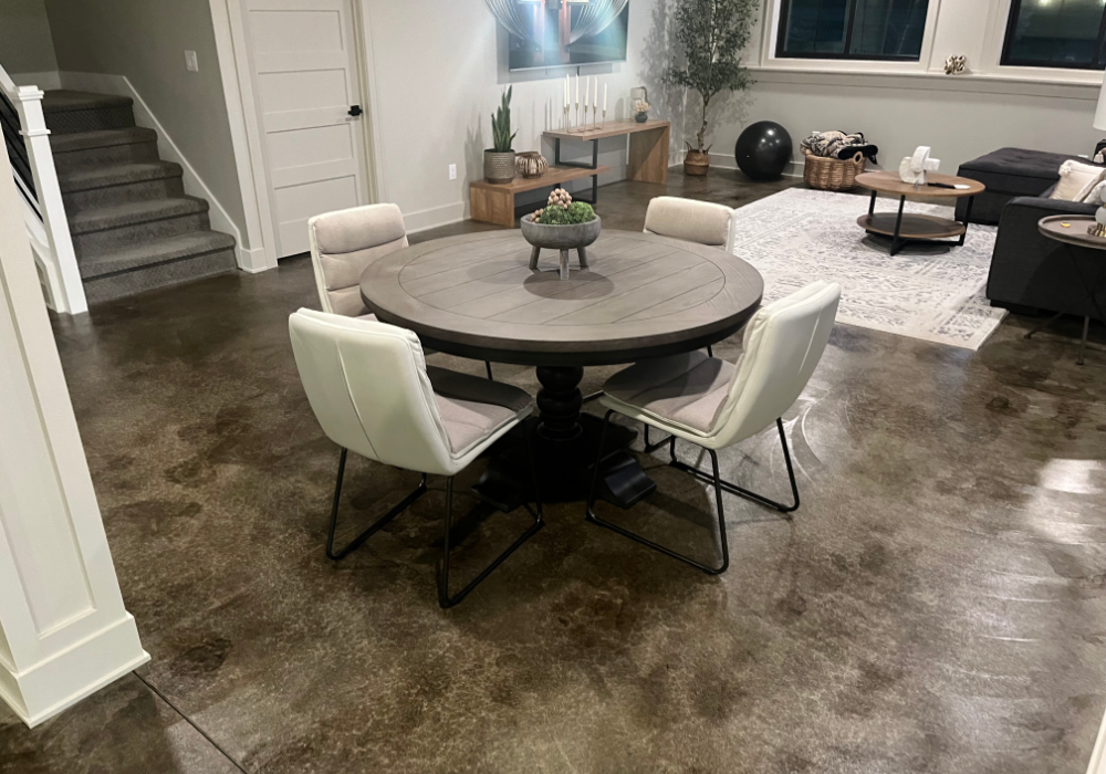 A finished basement living and dining area with a ColorWave Molasses stained concrete flor, modern furnishings, and soft lighting.