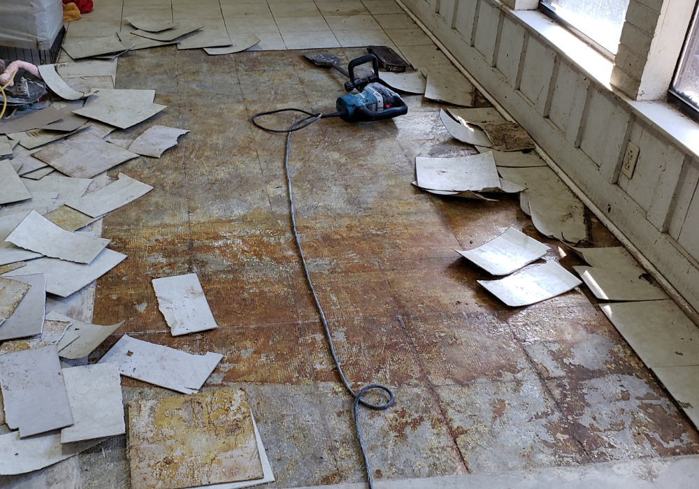 A game room floor in the process of PVC tile removal, revealing adhesive-stained concrete underneath