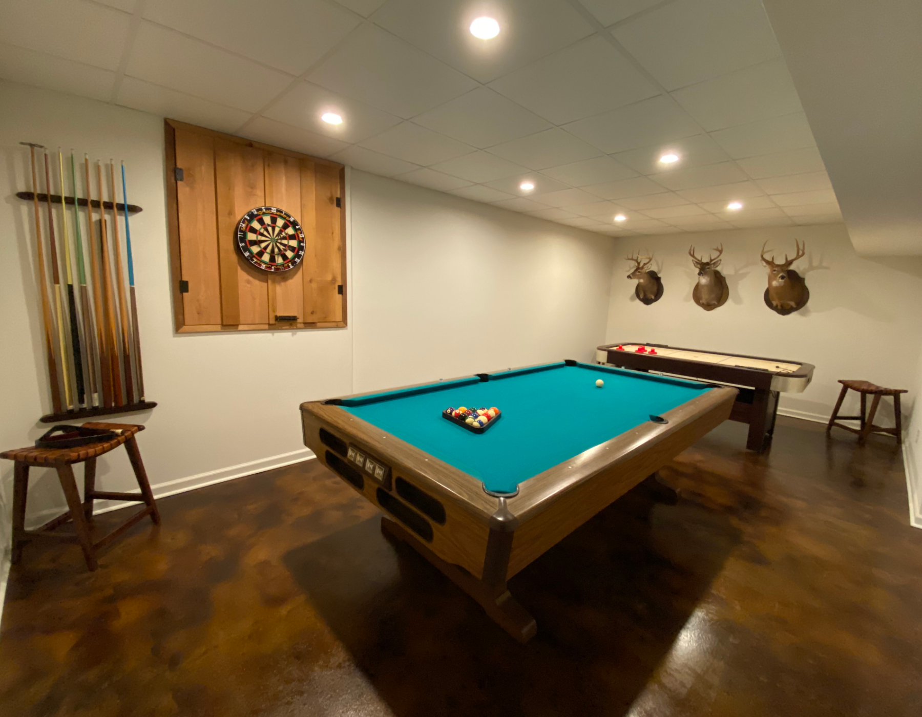 Renovated recreational room featuring an acid stained concrete floor, pool table, dartboard, and wall-mounted deer heads.