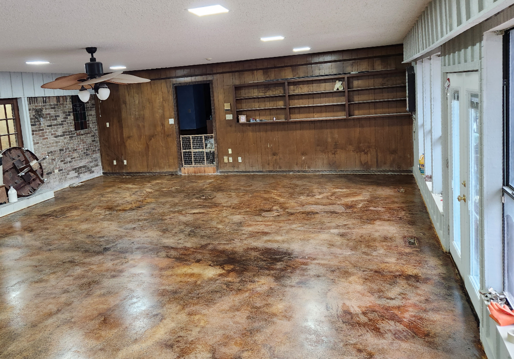 A stained concrete game room floor with Cola, Coffee Brown, and Desert Amber acid stains, featuring a smooth, leather-like finish