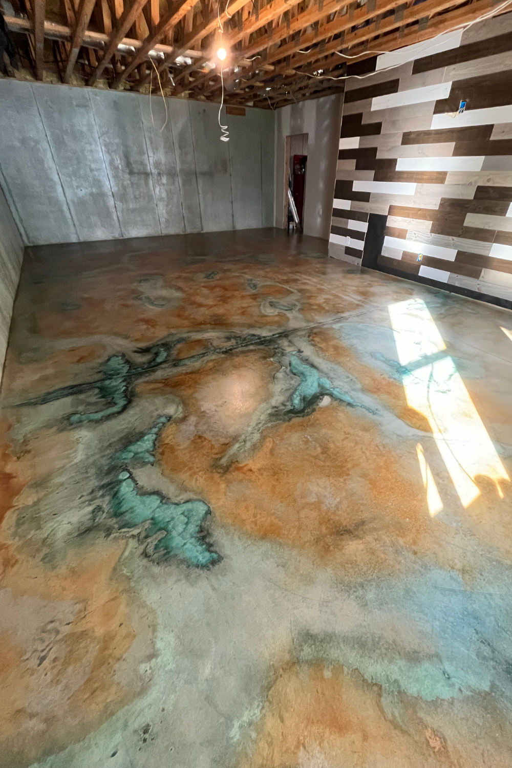 A finished man cave with a concrete floor stained using Malayan Buff and Seagrass, featuring bold blue veining patterns