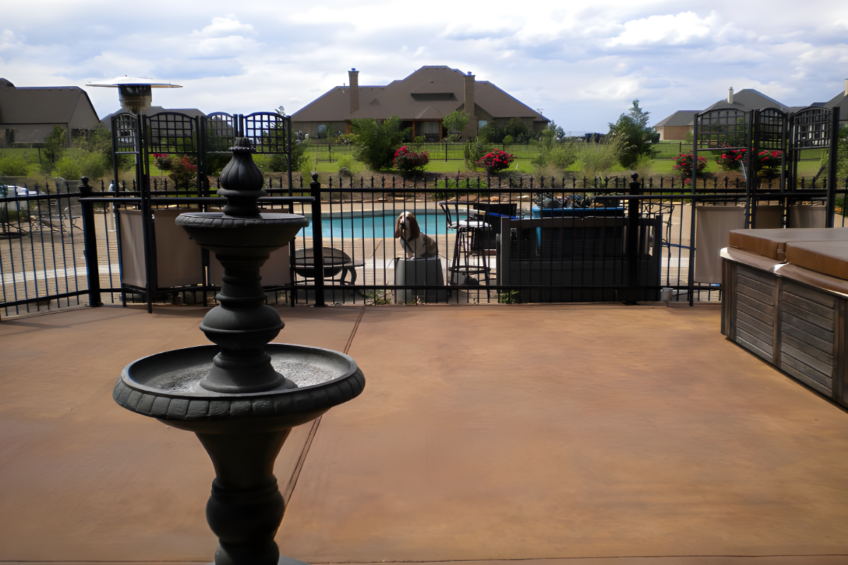 Broom-finished concrete patio stained with Caf Royale Antiquing Broom-finished concrete patio stained with Café Royale Antiquing™ Stain, featuring a rich, warm brown tone near a pool and fountain.