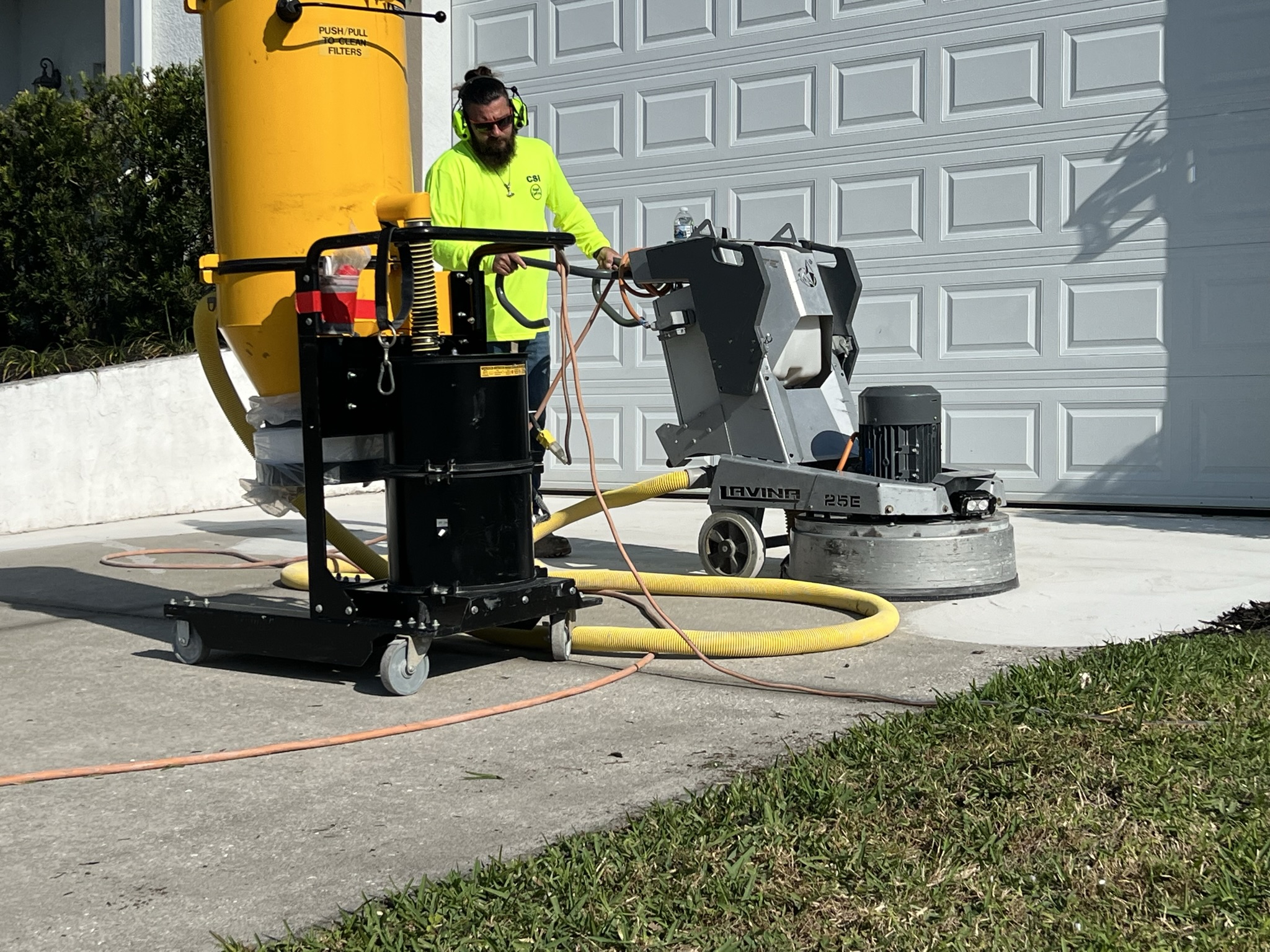 Contractor wearing protective gear expertly uses a grinder to smooth out the concrete driveway surface for a flawless finish