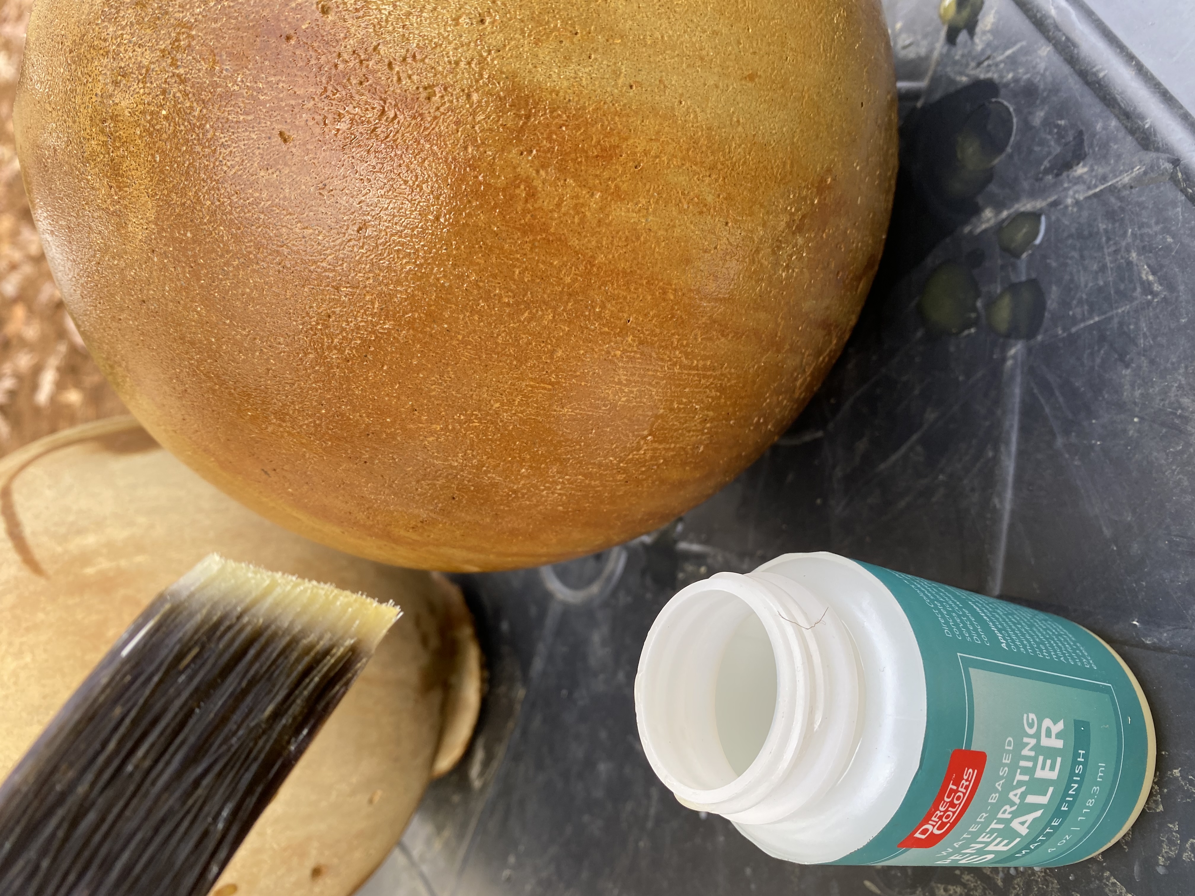 A photograph showcasing the application of a deep penetrating matte sealant using a paintbrush on a DIY spherical concrete fountain piece, previously stained with Malayan Buff and Desert Amber acid stain.