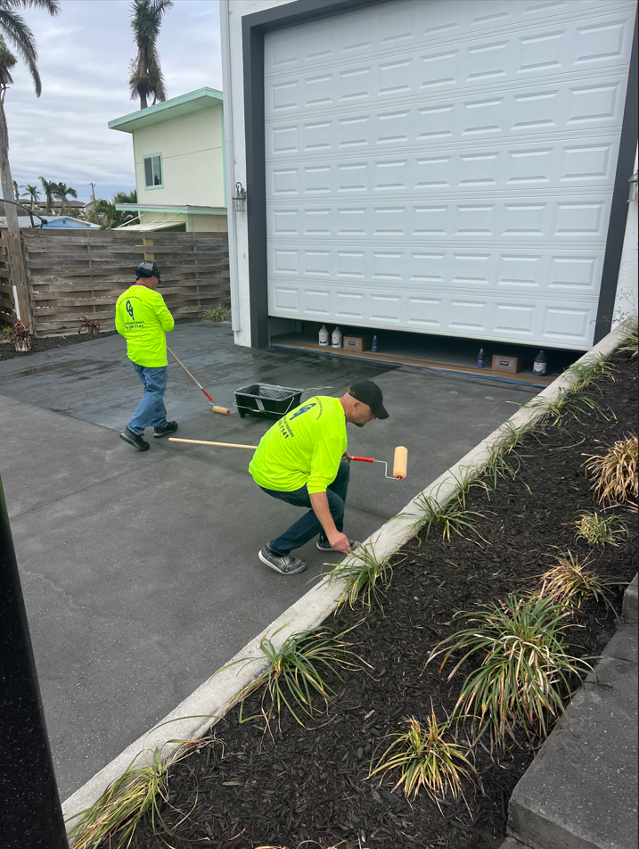 Contractors meticulously applying the second coat of EasySeal satin with a roller, enhancing the durability and protection of the Steel Gray ColorWave on the concrete driveway